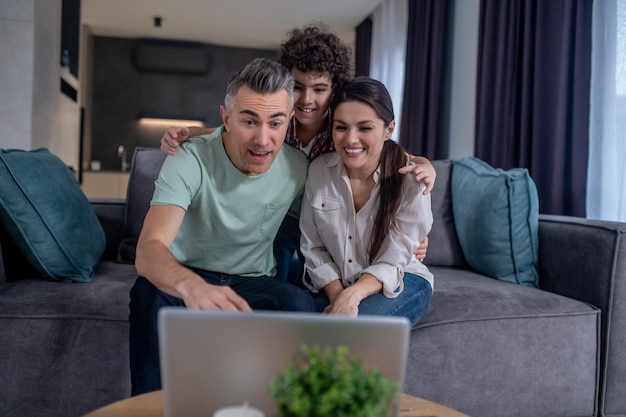 Boy hugging parents looking at laptop sitting on sofa