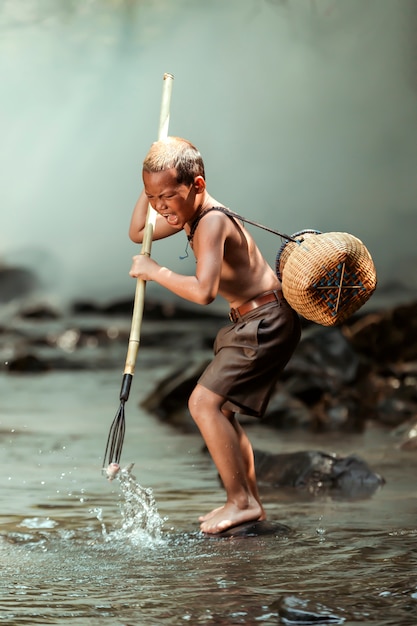 A boy is catching fish in a stream near his home. In the rural areas of Thailand