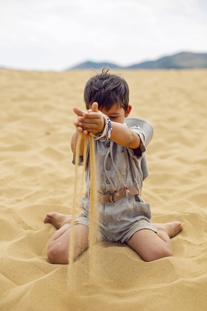 Boy is a child traveler in a suit of an archaeologist tracker and wearing hat sitting on the sand in the desert