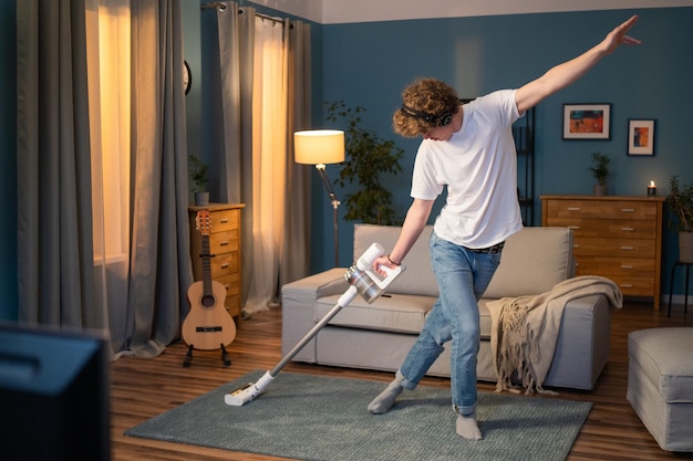 A boy is cleaning the living room in the evening the man has fun vacuuming the carpet in the room