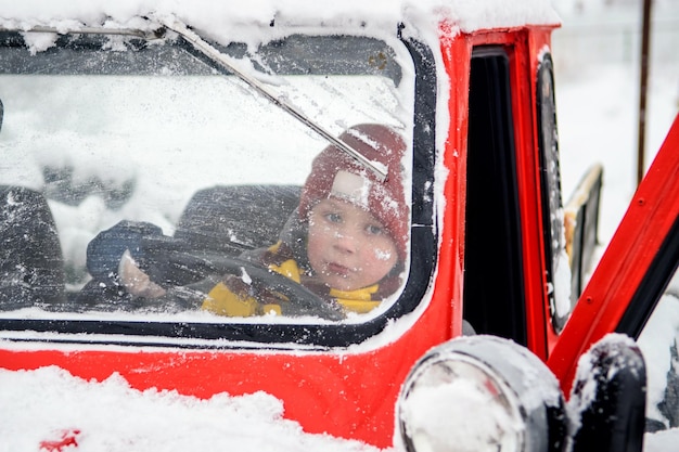 Boy is driving a red car with Christmas decorations in a winter forest. Festive New Year's concert.