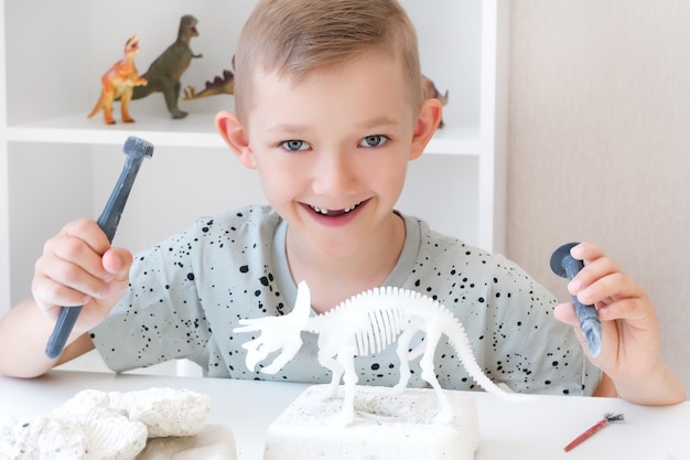 少年は恐竜の発掘に従事しています。子供との教育ゲーム。子供が恐竜の骨を掘り起こします。忍耐力と細かい運動能力の発達。幸せな少年