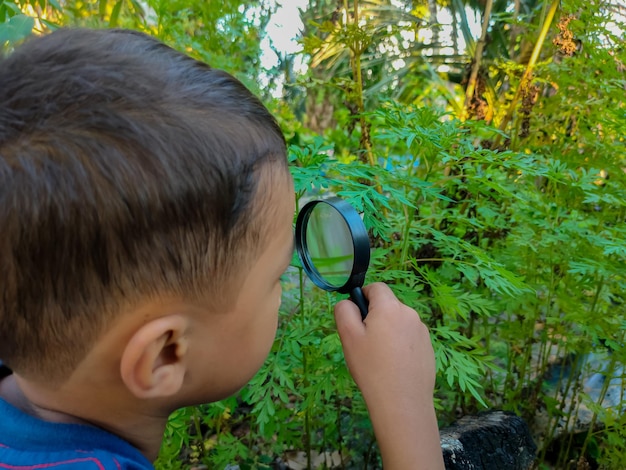 A boy is holding a magnifying glass while watching plants grow around his house