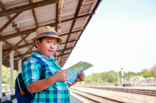 少年は電車が旅行するのを待っている地図を持っている。