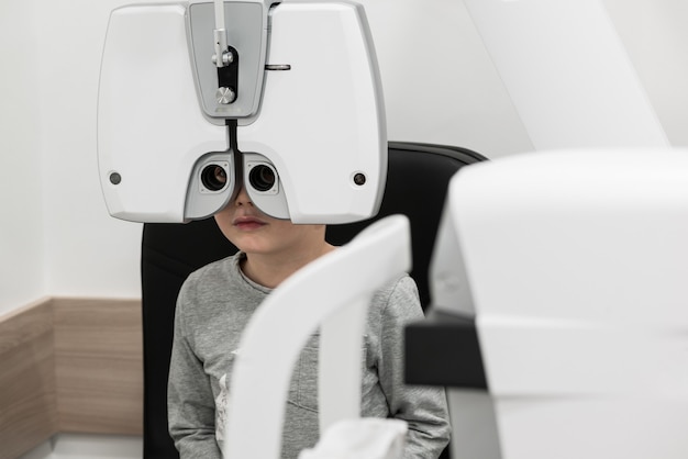 The boy is the patient on reception at doctor ophthalmologist diagnostic ophthalmologic equipment