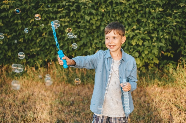 A boy is playing with soap bubbles in a summer park Among the greenery