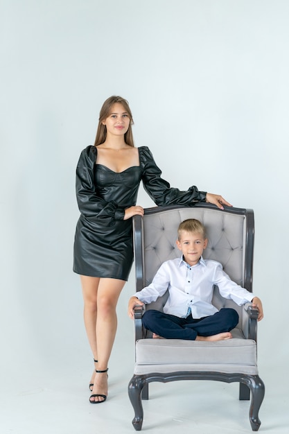 a boy is sitting in a chair a girl is standing next to him the most comfortable chair