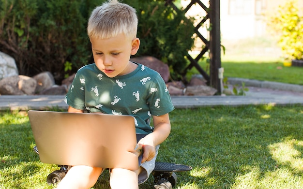 The boy is sitting on the grass and studying on a laptop.