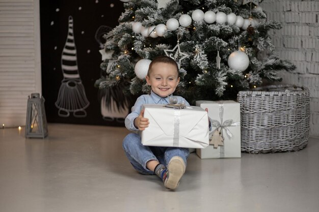 Foto il ragazzo è seduto e tiene in mano un regalo che aspetta che arrivi il nuovo anno per aprirlo tutto è decorato in modo luminoso per il nuovo anno