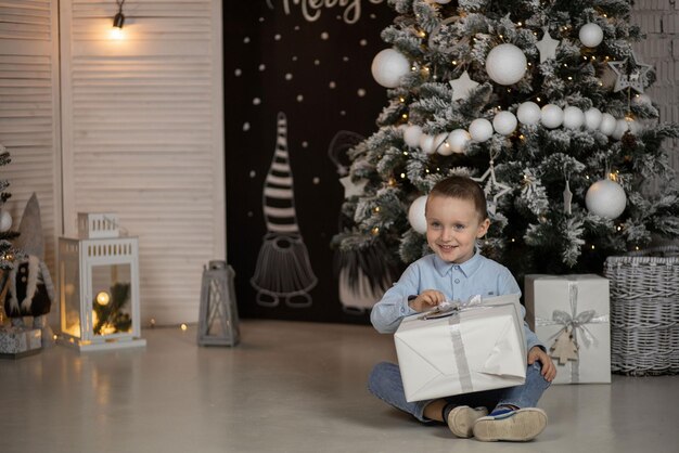 Foto il ragazzo è seduto e tiene in mano un regalo che aspetta che arrivi il nuovo anno per aprirlo tutto è decorato in modo luminoso per il nuovo anno