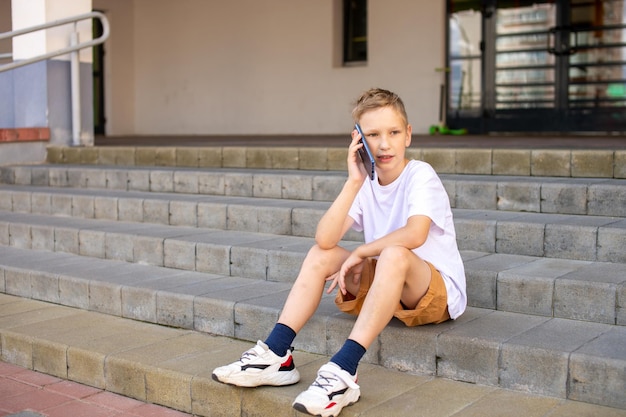 The boy is sitting on the steps and talking on the phone