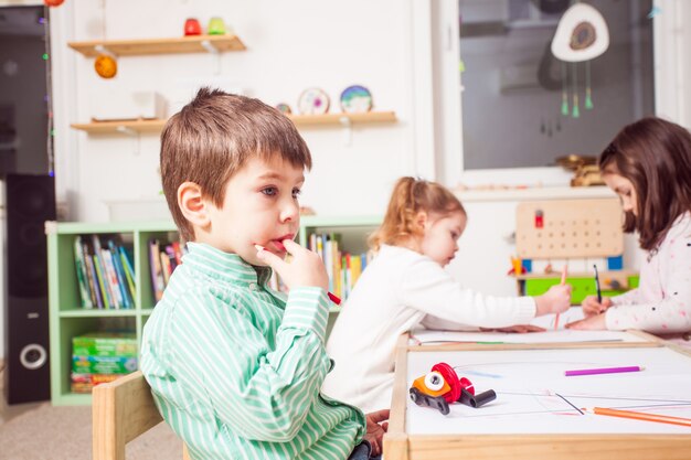 Boy is sitting and thinking what to draw in kindergarten