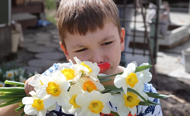 The boy is sniffing a bouquet of daffodil flowers in nature