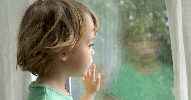 Boy is standing and looking out the window