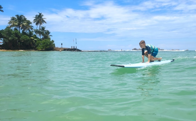 少年は美しいヤシの木のある青い海の砂浜で波の上をサーフィンしていますxA