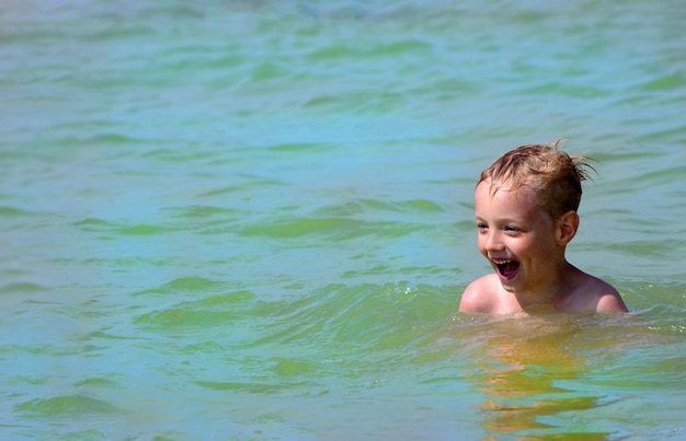 a boy is swimming in the water with a smile on his face.