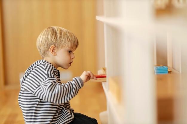 A boy is taking wooden educational toy form a shelf at kindergarten