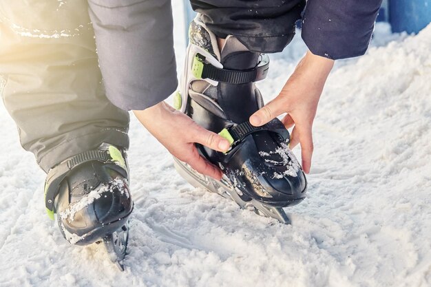 ジャケットとズボンの少年が雪の上に立ってアイス スケートを調整します。
