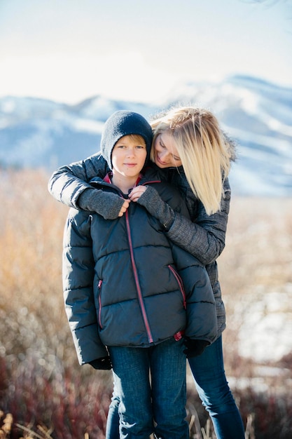 A boy in a jacket and woolly hat being hugged by his mother