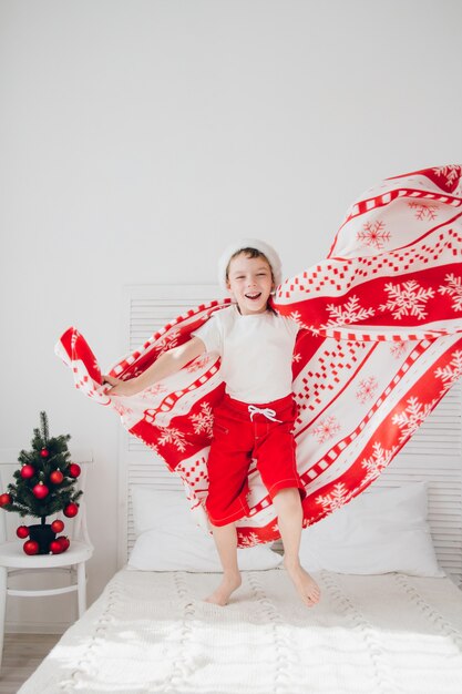 Boy jumping on the bed covered with a blanket