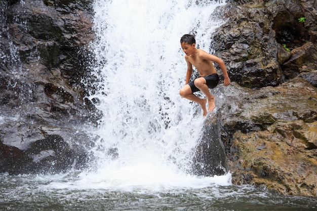 Boy jumping from rock into water in waterfall