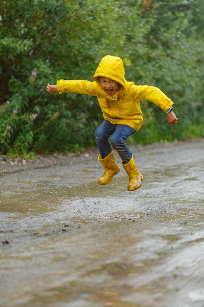 雨の中の泥だらけの池をジャンプする少年