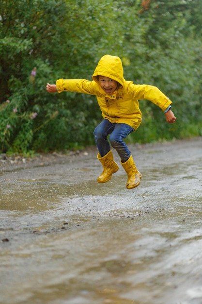 Photo boy jumping through muddy puddles in the rain