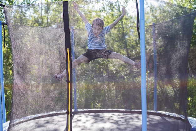 トランポリンでジャンプする男の子子供は屋外のトランポリンで遊ぶ