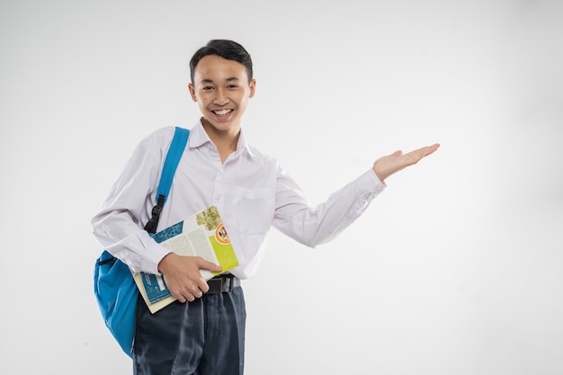 Un ragazzo in uniforme della scuola media che offre qualcosa con un gesto delle mani quando porta un libro