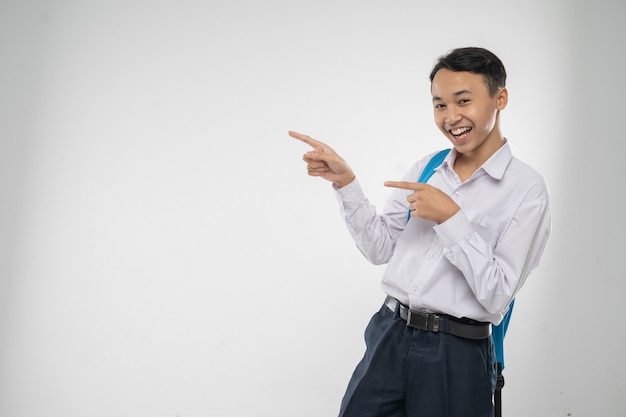 A boy in junior high school uniform smiling with finger pointing when carrying a backpack with copys...