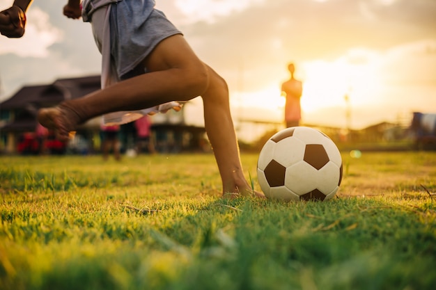 Boy kicking a soccer ball with bare foot on the green grass field