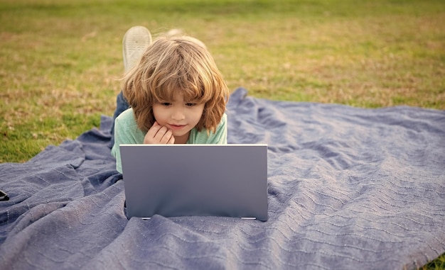 Boy kid use laptop computer learning technology relaxing on blanket natural outdoors online courses