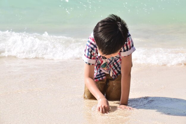 Foto ragazzo in ginocchio sulla sabbia sulla spiaggia