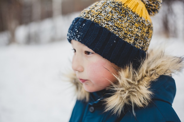 A boy in a knitted scarf and a warm jacket on a walk in the winter in the Park or forest