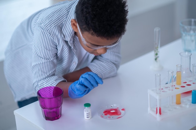 A boy in a lab coat working with test tubes and looking involved