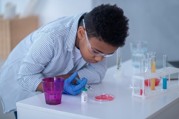 A boy in a lab coat working with test tubes and looking involved