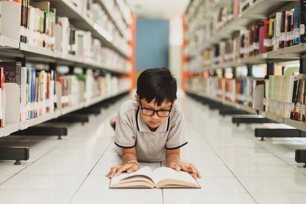 Boy laying down on the floor reading a book in library Education concept