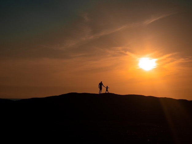 소년은 언덕을 통해 태양을 향해 아버지를 이끈다 아름다운 일몰 실루엣