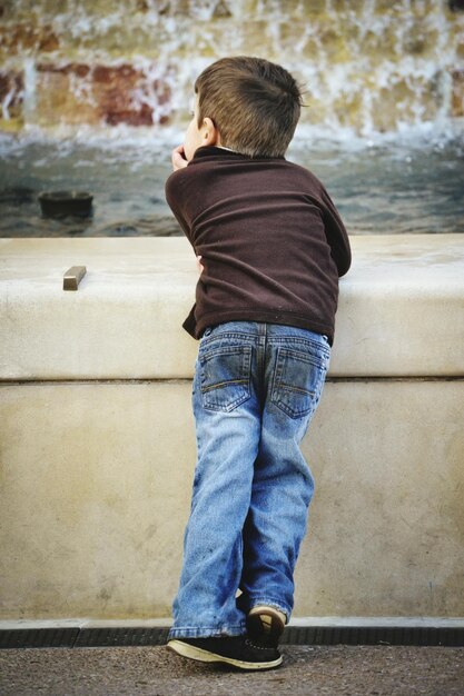 Photo boy leaning on wall against fountain