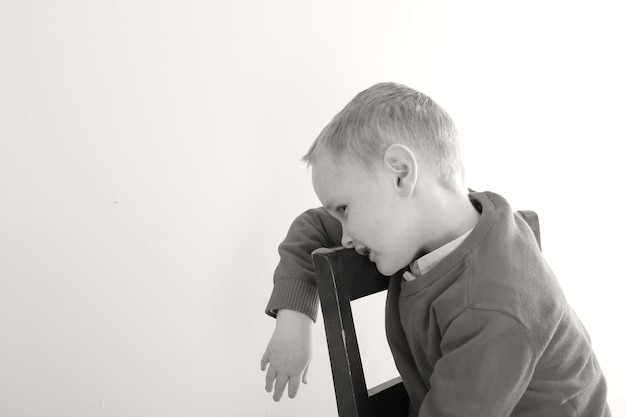 Photo boy leaning while sitting on chair against wall