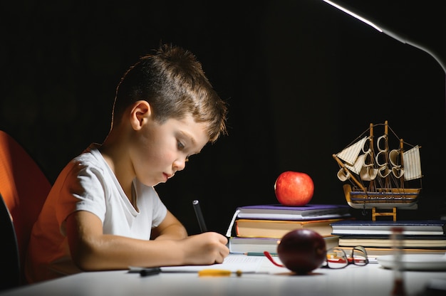 Boy learn lessons in the home setting at the table in the light of a table lamp.