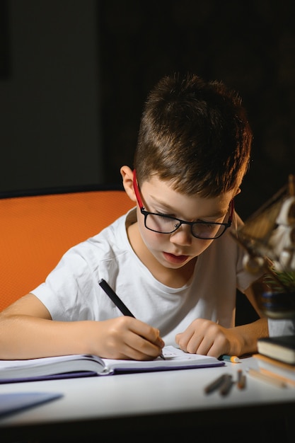 Boy learn lessons in the home setting at the table in the light of a table lamp.