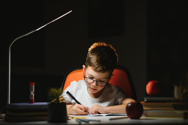 Photo boy learn lessons in the home setting at the table in the light of a table lamp.