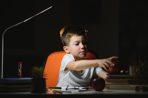 Photo boy learn lessons in the home setting at the table in the light of a table lamp.