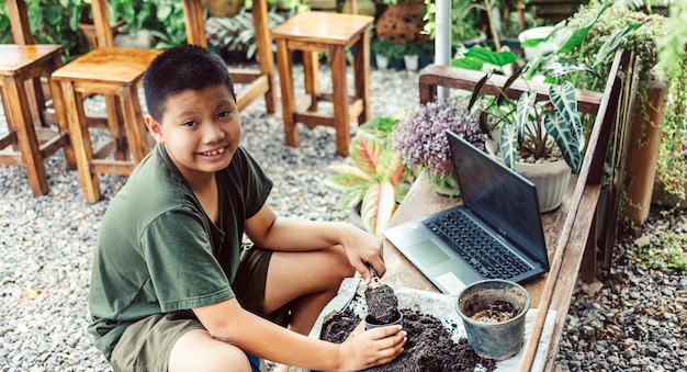 Мальчик учится выращивать цветы в горшках с помощью онлайн-обучения засыпать почву лопатой в горшки для подготовки растений.