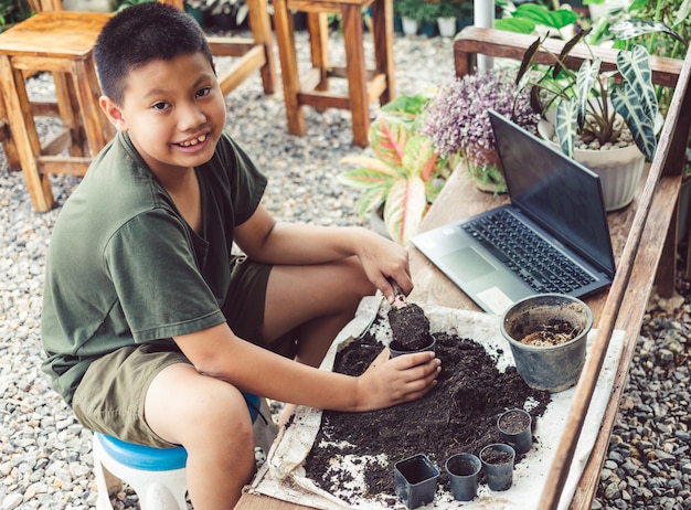 The boy learns to grow flowers in pots through online teaching shoveling soil into pots