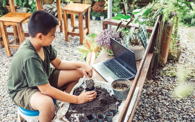 Мальчик учится выращивать цветы в горшках с помощью онлайн-обучения засыпать землю лопатой в горшки