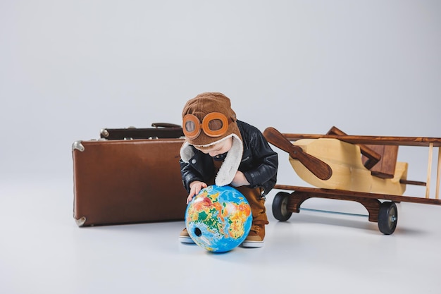 Мальчик в кожаной куртке и шапке пилота деревянный самолет глобус коричневые чемоданы Детские деревянные игрушки