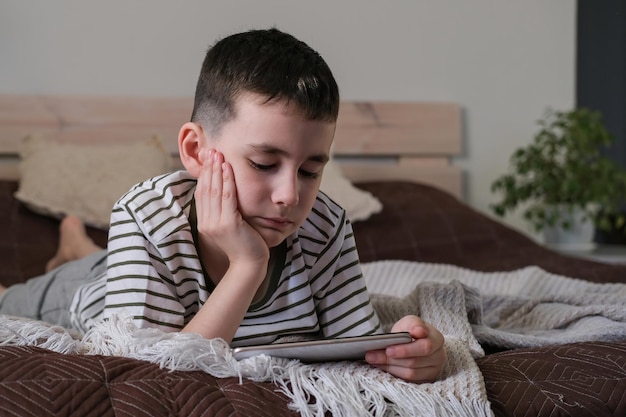 The boy lies on the bed and watches a cartoons and video on a smartphone