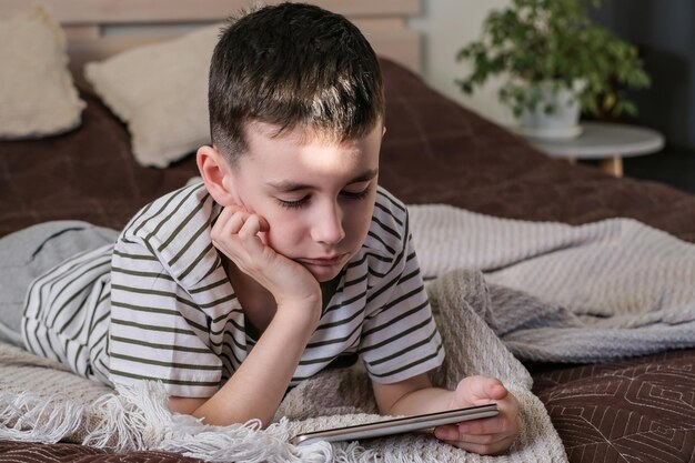 The boy lies on the bed and watches a cartoons and video on a smartphone